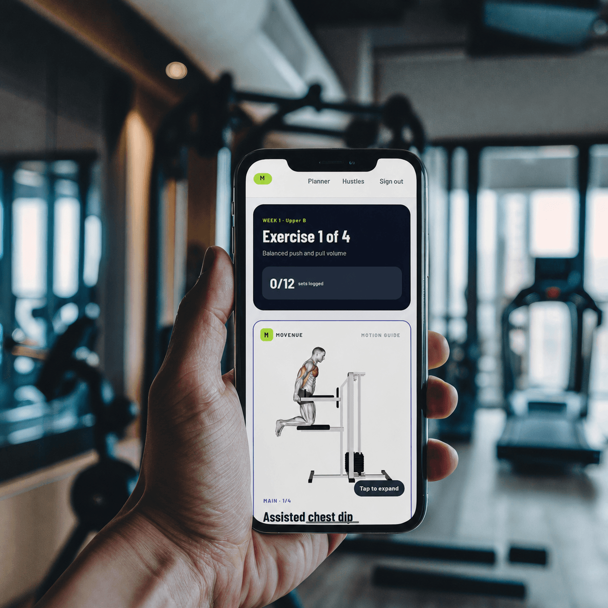 A member holding a phone showing a Movenue assisted chest dip machine workout